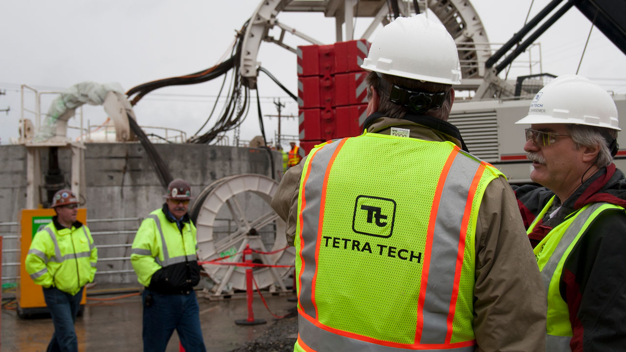 Workers in high-visibility safety gear and hard hats in front of construction equipment at a project site