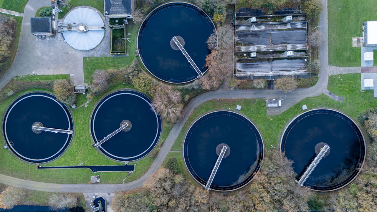 Top-down aerial view of a wastewater treatment plant with circular clarifier tanks and water basins