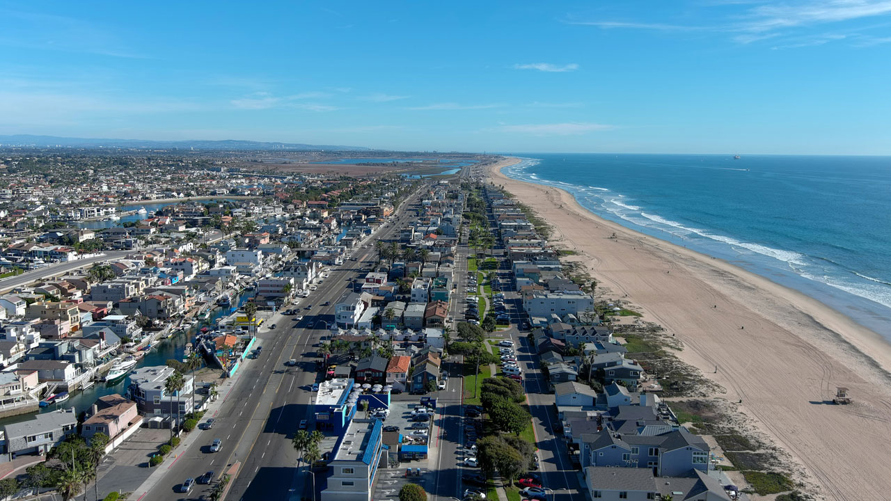 Aerial view of Huntington Beach with a long sandy beach, oceanfront homes, and a busy main road